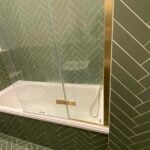A walk-in shower with green herringbone tiles, designed by a bathroom fitter, and a clear glass door.