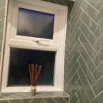 A frosted glass window on a tiled bathroom wall with aroma diffuser reeds on the sill, designed for a disabled bathroom.