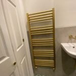 A gold towel warmer is leaning against a wall in a disabled bathroom with a white door and sink.
