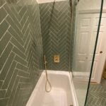 A modern bathroom design with a herringbone-tiled shower and a glass door.