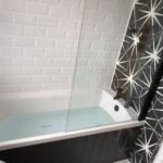 A modern bathroom installation featuring a white subway-tiled wall, a glass shower panel, and a bathtub with a black and white patterned shower curtain.