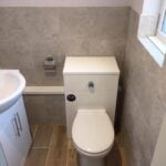 A modern disabled bathroom with beige tiling, featuring a closed toilet and a basin cabinet.