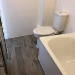A small disabled bathroom with a toilet adjacent to a bathtub, featuring gray flooring and white walls.