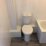A disabled bathroom toilet installed with limited legroom due to its proximity to a shower enclosure.