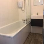 A modern disabled bathroom with a white bathtub and a glass shower screen.