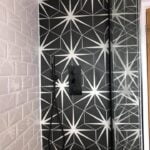 Modern bathroom design with a geometric-patterned shower wall and black fixtures.