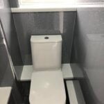 A modern white toilet in a disabled bathroom with gray speckled walls.