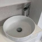 A white countertop basin with a modern tap, set against a light-colored bathroom tiling backsplash.
