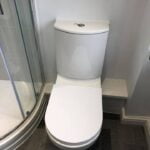 A white toilet located next to a glass shower enclosure in a disabled bathroom with gray tiled flooring.