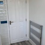 A white door next to a towel radiator in a clean, modern bathroom awaiting its final touches from a skilled bathroom fitter.