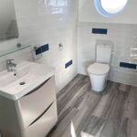Modern disabled bathroom interior with white and blue tiles, a sink, and a toilet under natural light.