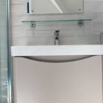 White disabled bathroom sink with chrome faucet against a tile wall, flanked by glass shelves.