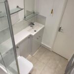 Modern disabled bathroom design with a glass shower enclosure, white basin, and toilet.