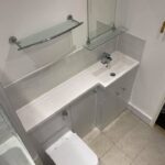 Modern disabled bathroom interior featuring a wall-mounted toilet, a sink with a single faucet, and a glass shelf above the sink.
