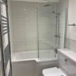 Modern bathroom design featuring a glass shower screen, white subway tiles, a bathtub, a toilet, and a heated towel rail.