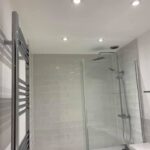 A modern bathroom design with a glass shower cubicle, white subway tiles, and a towel warmer.