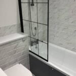 Modern bathroom design with a glass shower screen, white tiles, and grey cabinets.