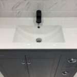 Modern white bathroom sink with a matte black faucet set against a marble-tiled wall, customized by a bathroom fitter for an optimal disabled bathroom design.