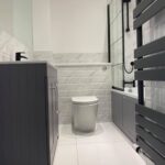 A modern, disabled-friendly bathroom with gray cabinetry, white walls, and a heated towel rail.