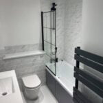 Modern bathroom installation featuring a walk-in shower, white fixtures, and gray tiles designed for disabled accessibility.