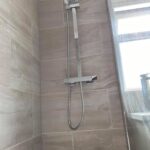 Modern shower with wall-mounted showerhead, glass door, and accessible features for a disabled bathroom.