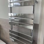 Stainless steel bathroom towel radiator mounted on a wall beside a toilet, installed by a professional bathroom fitter.