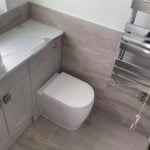 A modern disabled bathroom with a gray vanity unit, wall-hung toilet, and heated towel rail.