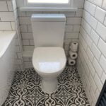 Modern bathroom interior featuring a white toilet against a tiled wall with patterned flooring, expertly installed by a professional bathroom fitter.