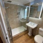 Modern disabled bathroom interior with a glass shower enclosure, wall-mounted sink, and toilet.