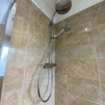 A dual shower head system installed in a tiled shower stall, optimized for disabled bathroom use.