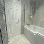 Modern bathroom with a glass shower screen, disabled bathroom features, white bathtub, and tiled walls.