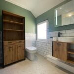 A modern disabled bathroom with green walls, a wooden vanity, and white subway tiles.