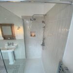 A bright, clean bathroom with a walk-in shower, white tiles, metallic fixtures, and designed for disabled access.