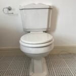 A white toilet designed for a disabled bathroom, against a wall with tiled flooring.