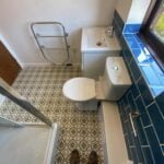 Compact disabled bathroom with a patterned floor, white fixtures, and blue tiles.