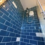 Modern bathroom design features a corner with blue tiles and a glass shower enclosure, tailored for disabled bathroom needs.