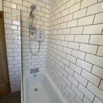 A modern disabled bathroom with white subway tiles and a fitted bathtub with a shower system.