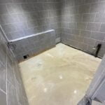A newly tiled disabled bathroom experiencing flooding due to water accumulation on the floor.