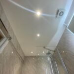 Upside-down view of a disabled bathroom with glass shower enclosure and recessed ceiling lights.