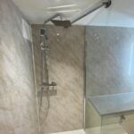 A modern bathroom installation featuring a shower with adjustable head mounted on a marble-tiled wall.