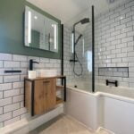 Modern bathroom interior with subway tiles, a glass shower partition, wooden vanity, an illuminated mirror, and disabled bathroom features.