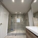 Modern disabled bathroom interior with walk-in shower and wooden vanity.