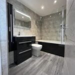 A modern disabled bathroom with a walk-in shower, vanity cabinet, toilet, and tiled walls and flooring.