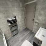 A modern disabled bathroom with grey tiles, featuring a shower cubicle, a toilet, and a heated towel rail.