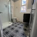 A modern bathroom design with white subway tiles, patterned floor tiles, a corner shower stall, and a black vanity.