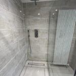 A modern walk-in shower with beige tiles and a wall-mounted radiator, expertly completed by a professional bathroom fitter.
