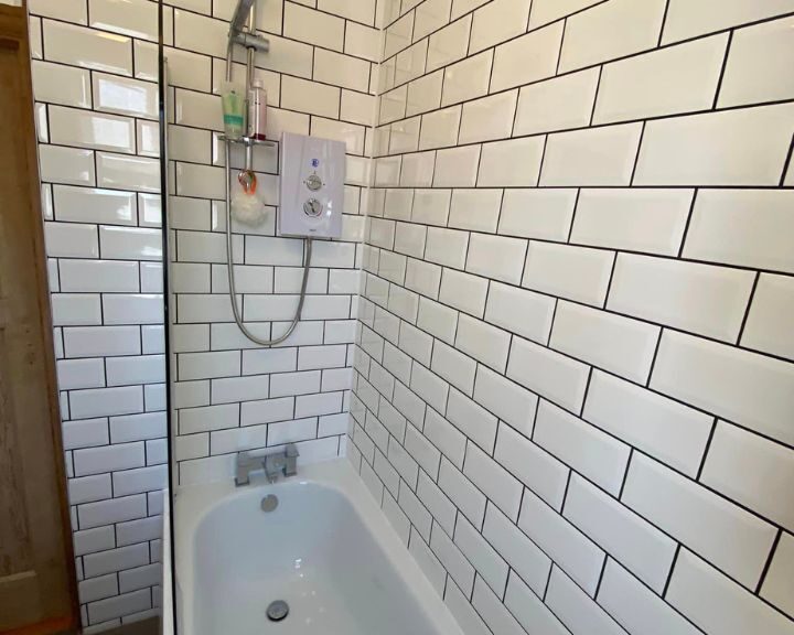 A white-tiled bathroom design with a bathtub and a wall-mounted shower system.