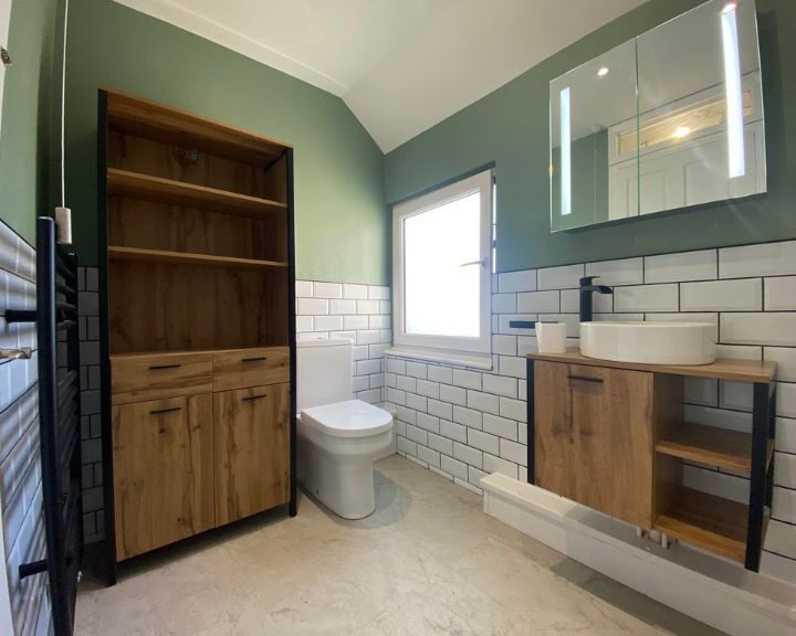 Modern bathroom installation with green walls, white subway tiles, wooden vanity units, and a wall-mounted toilet.