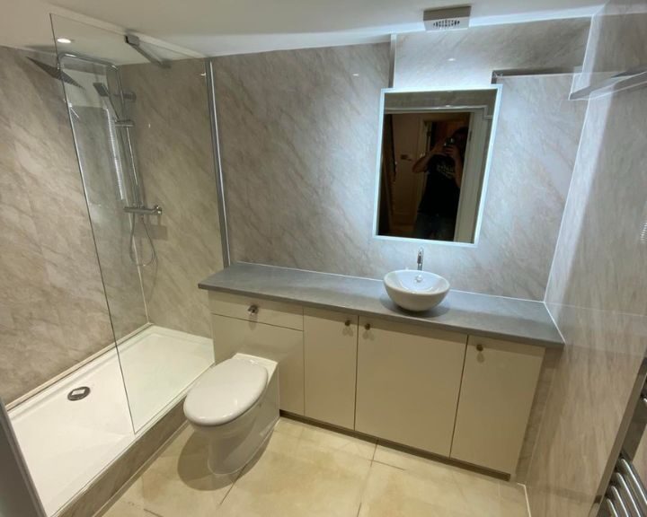 A modern disabled bathroom with a shower stall, toilet, and vanity, including a mirrored reflection of someone taking the photo.