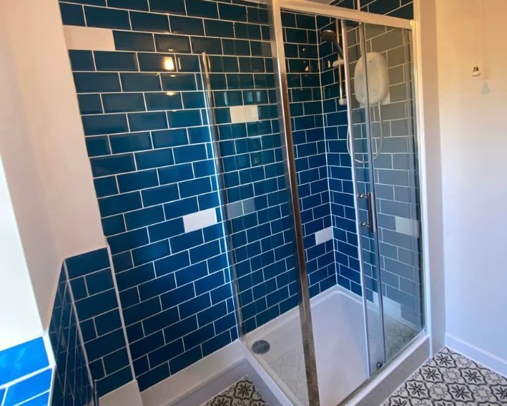 A modern disabled bathroom corner with a glass shower enclosure and blue tiled walls.